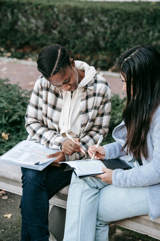 pexels-photo-5965714-5965714 Concentrated diverse female students in casual outfits working on home assignment together and sitting on bench in park